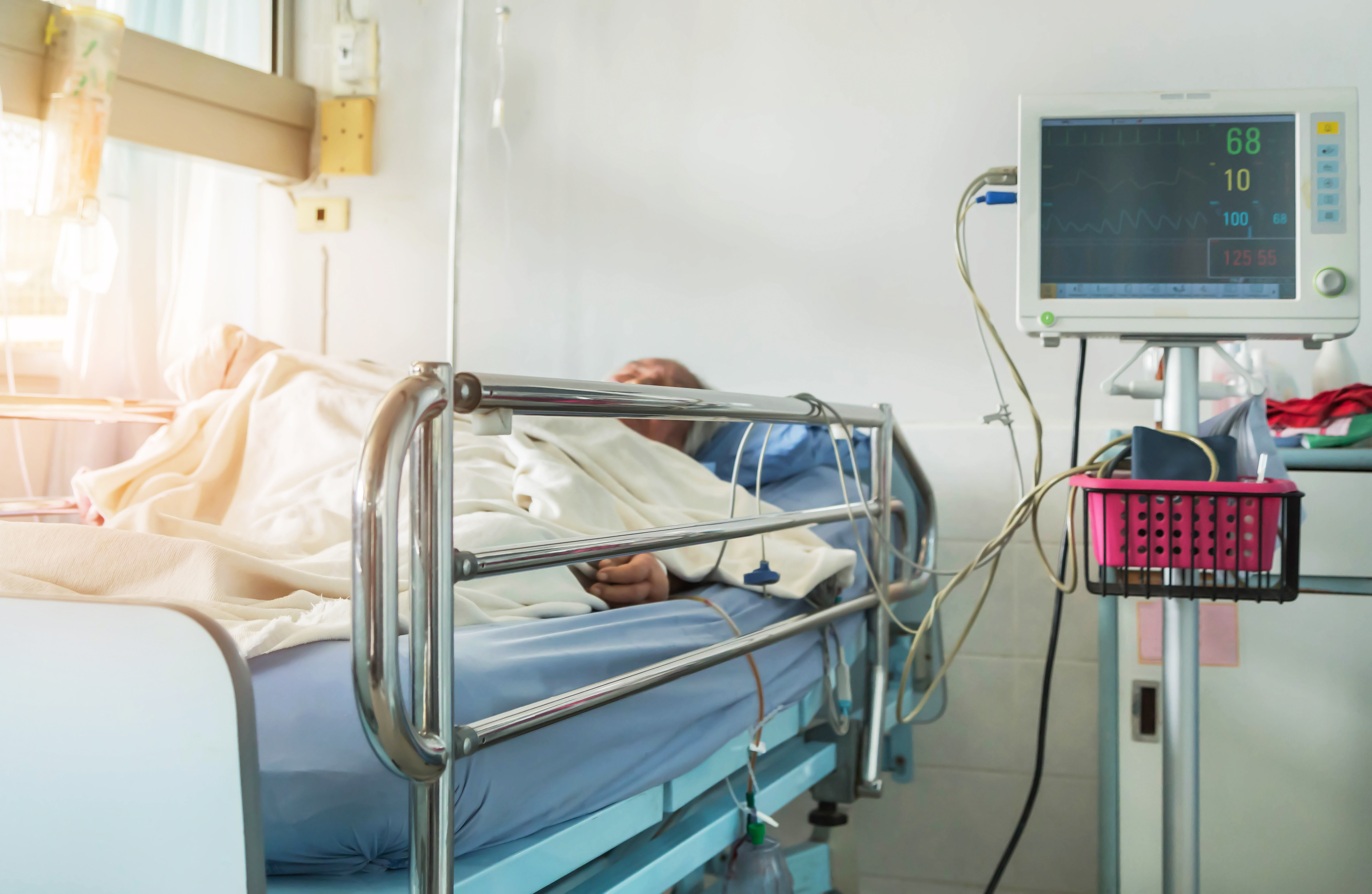 an older adult is in a hospital bed with bed rails hooked up to a monitor to one side providing fall technology. 