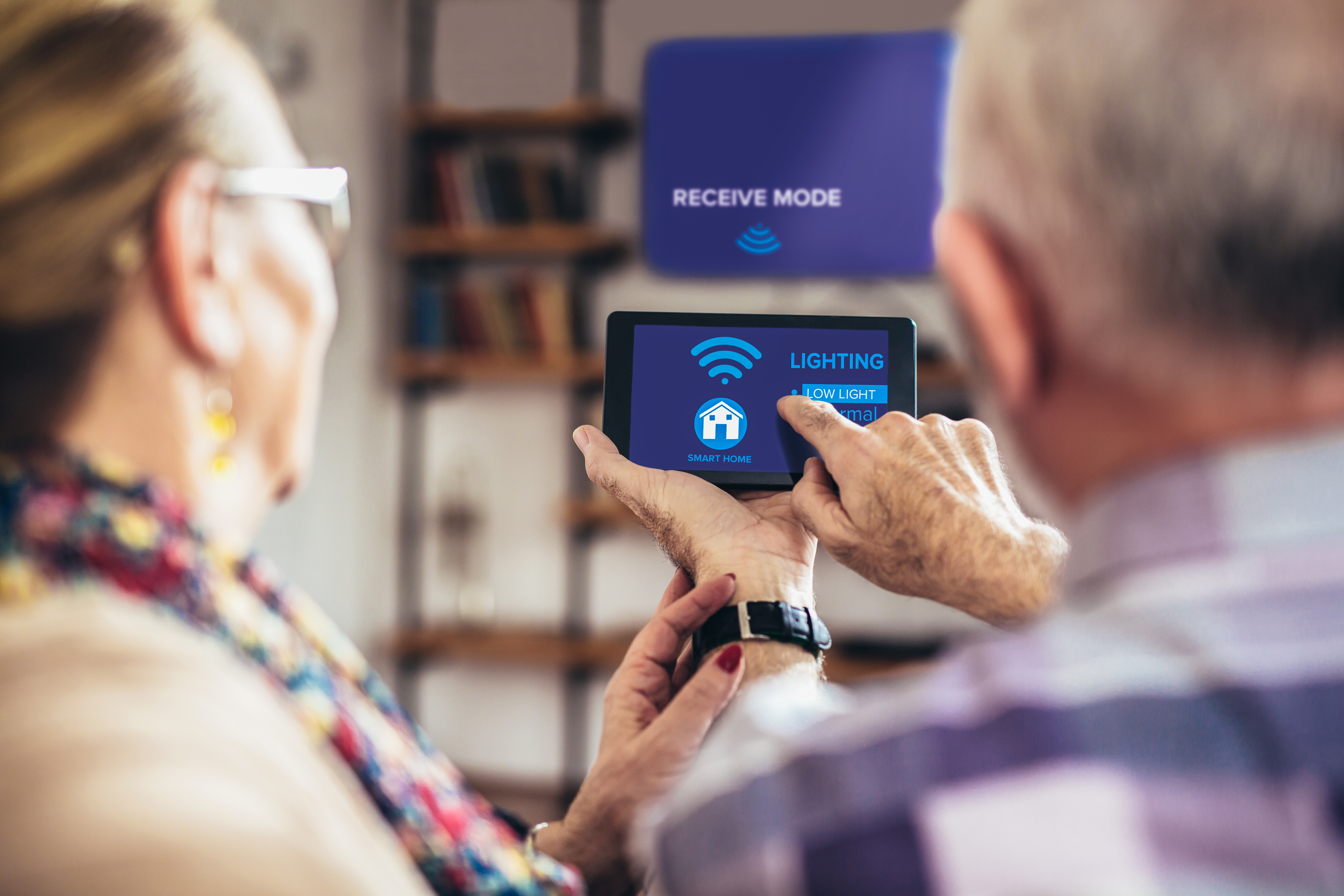 two older adults sit with the digital remote to their smart home settings 