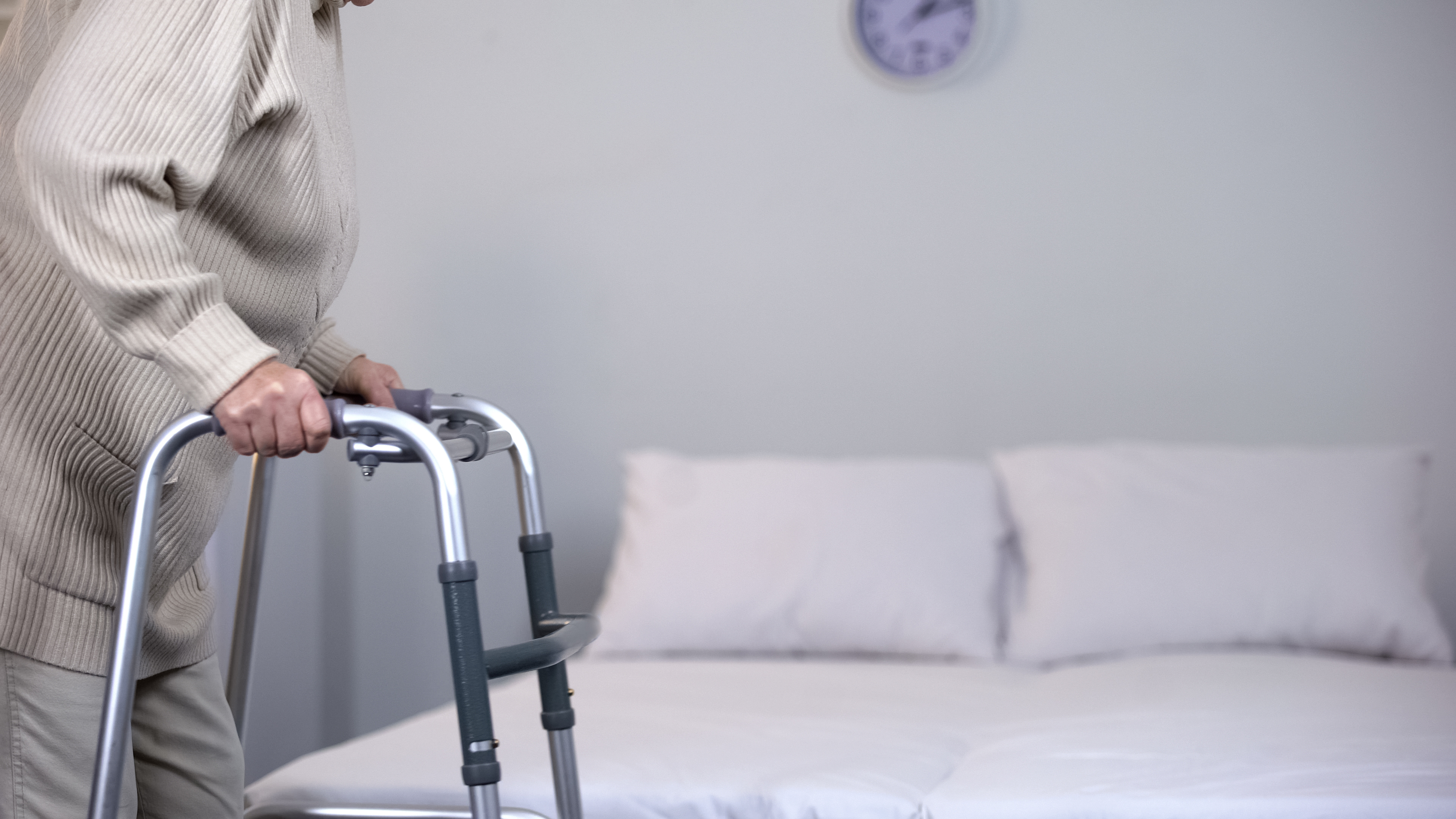 senior woman uses a walker for stability near a clean bed 