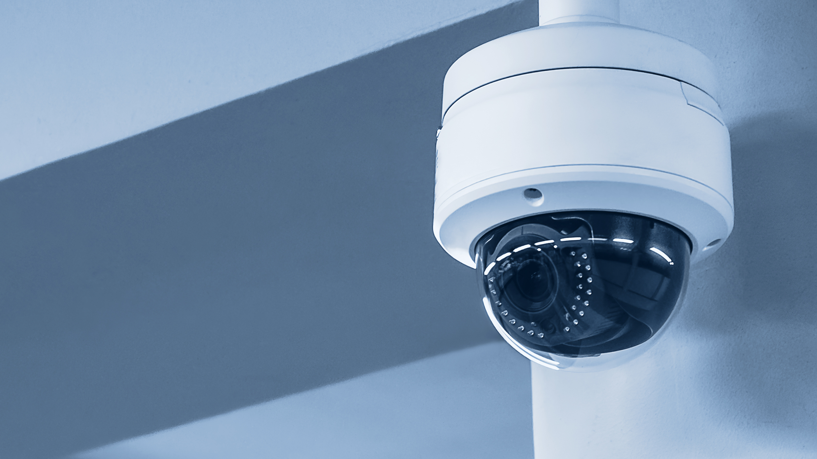 a white surveillance camera hangs from the ceiling in a gray room 