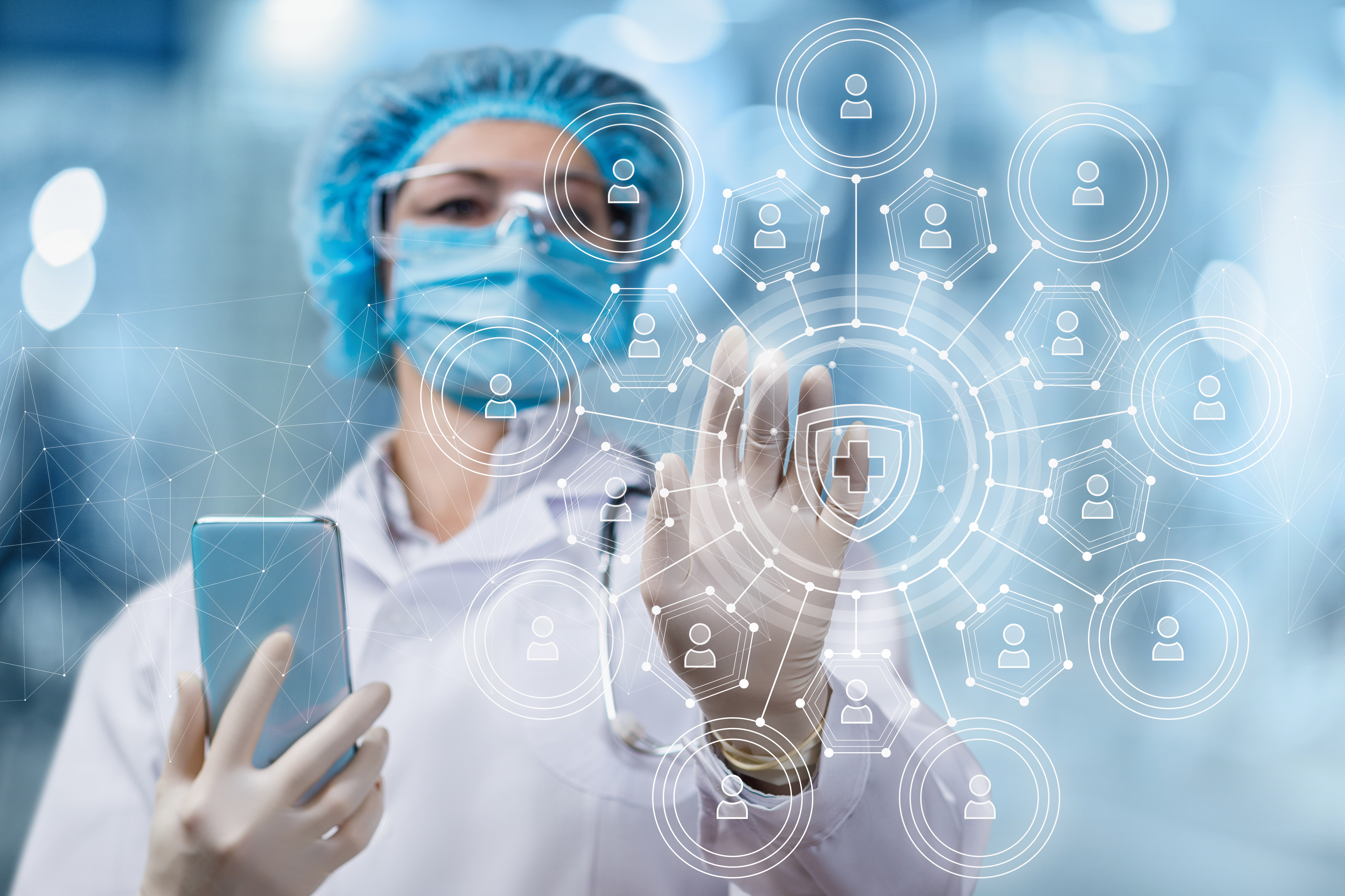 A healthcare worker in full scrubs and mask holds a cell phone and reached toward the viewer to interact with a translucent technical overlay.