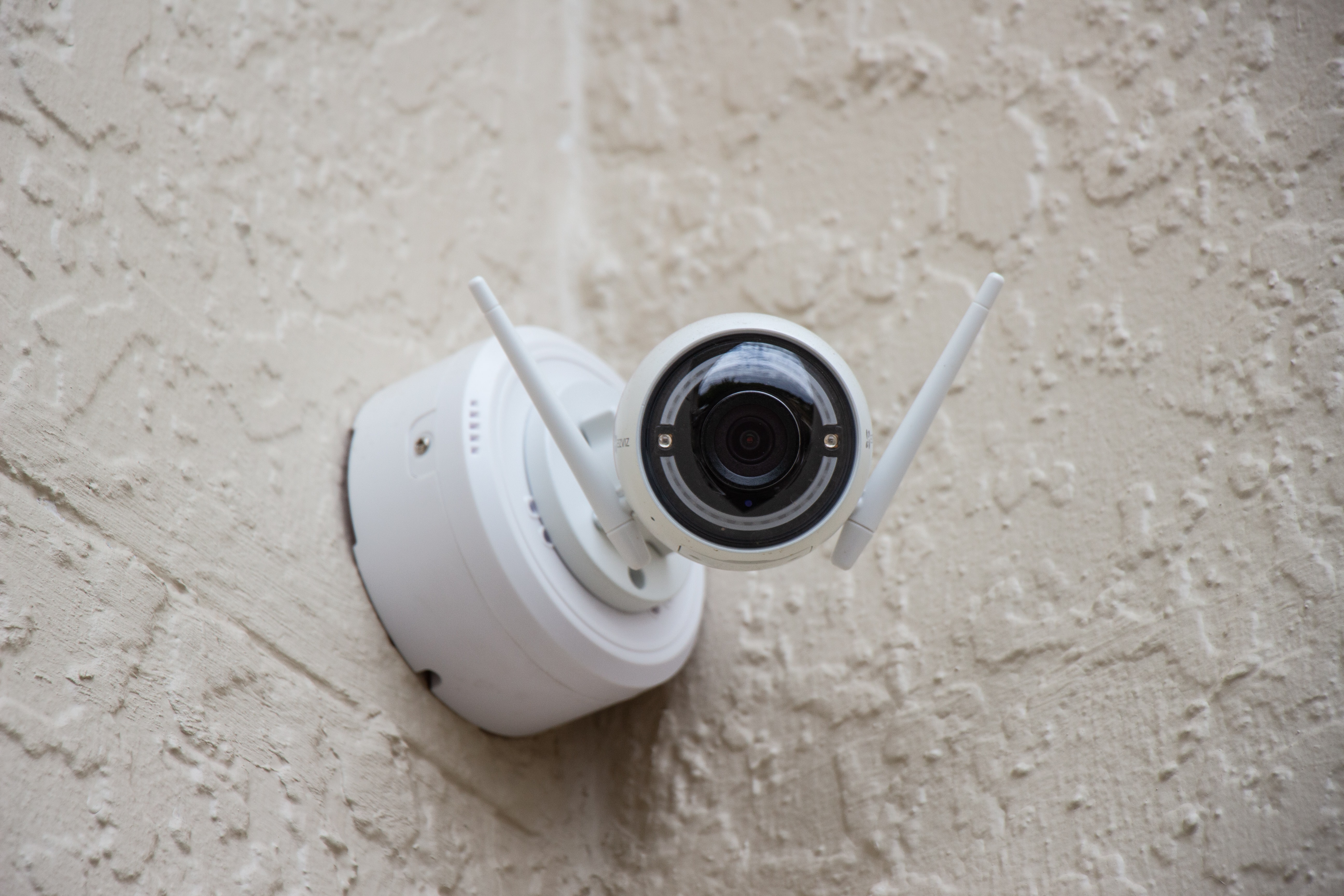 Photo of a small, white security camera on a orange-peel textured gray wall 