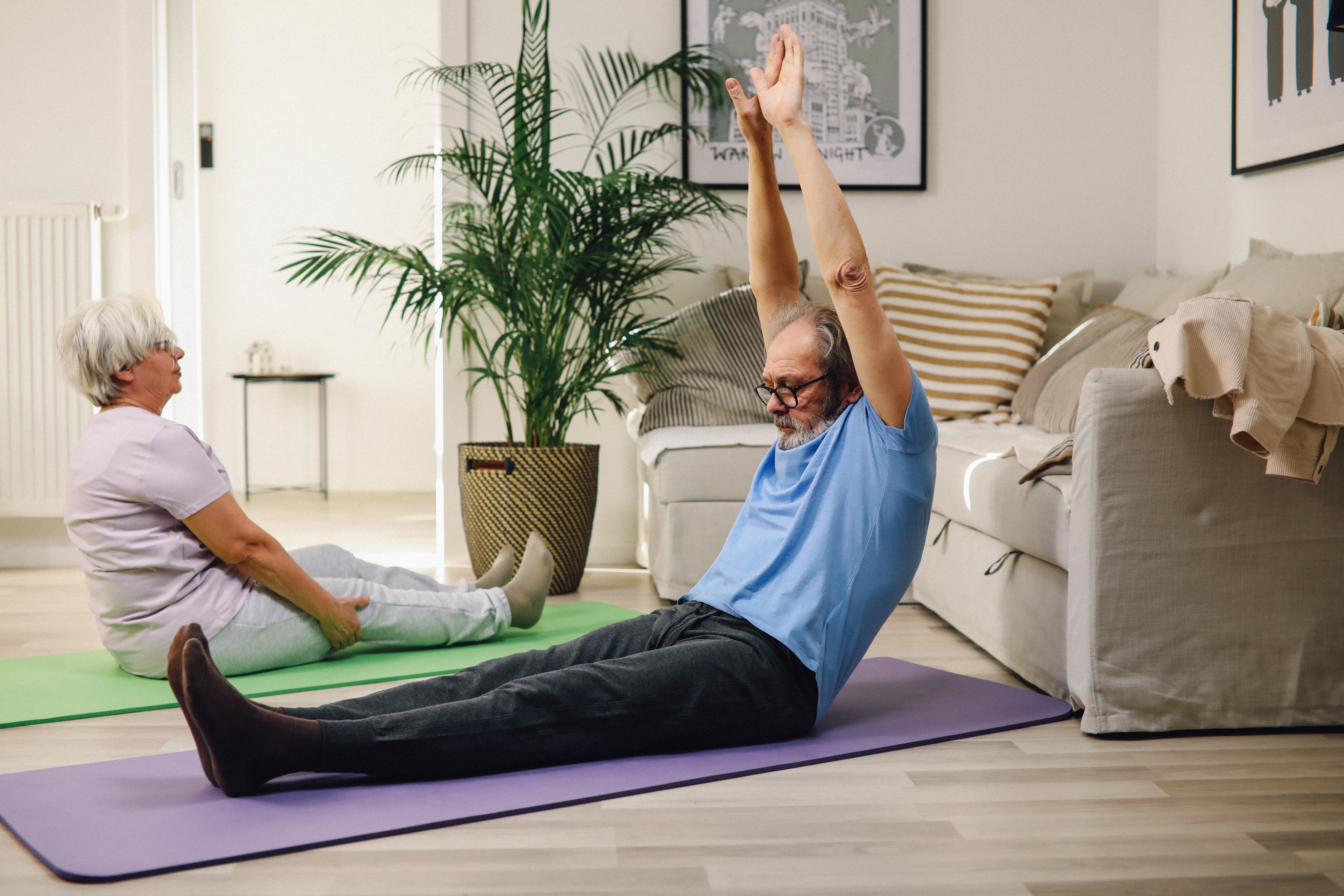 Two older adults stretching together in a living room. 