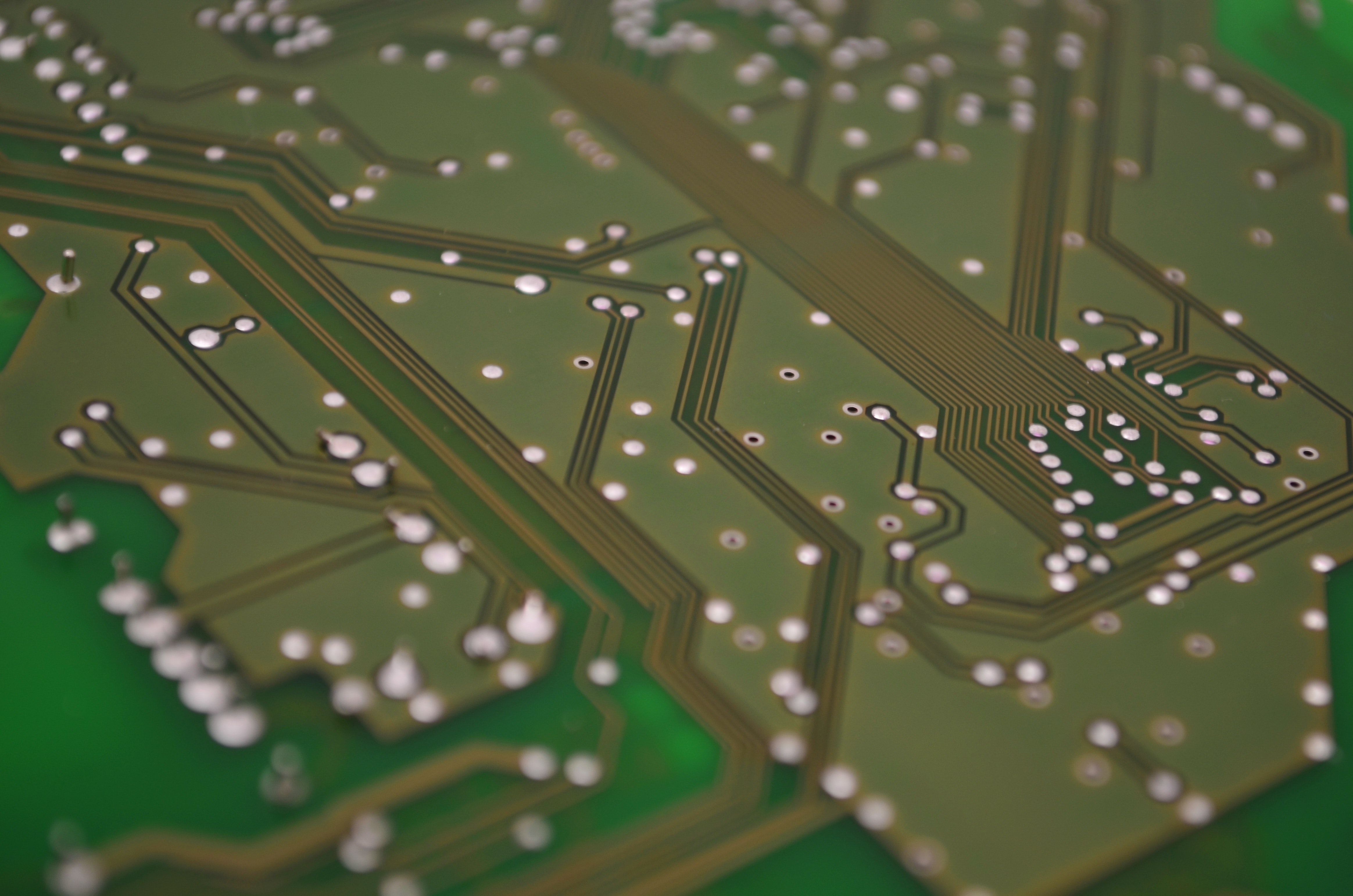 close up image of a green circuit board with silver grommets and brass pathways 